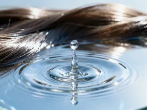 Pojedyncze mokre pasmo włosów zwinięte w naturalny spiralny skręt na białym tle, ilustrujące potencjał włosów do kręcenia.